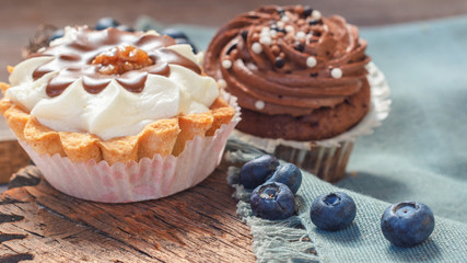 Obraz na płótnie Canvas cupcakes with chocolate and butter cream on a wooden background with blueberries scattered