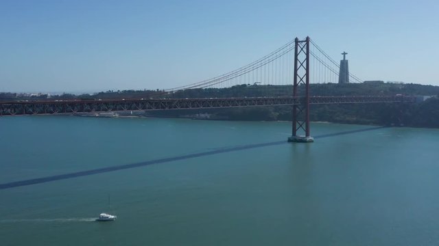 boat driving under the 25 Of April (Ponte 25 De Abril) Bridge over the Tagus River aerial drone reveal shot in Lisbon, Portugal Liboa
