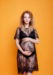 Fototapeta premium pregnant young beautiful fashion blonde model woman in studio in black underwear on yellow orange background