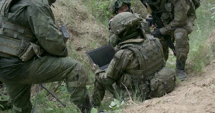 Soldiers in camouflage in ambush, military engineer uses a laptop navigation system, military action in the steppe area.
