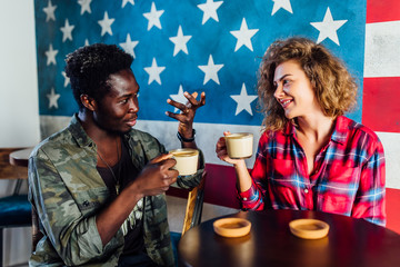 Cheerful male and female teen best friends sitting on cafe terrace drinking coffee and joking, romantic couple in love dressed in casual wear having fun during date communicating and resting ..