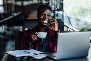 Handsome model, african young man working on laptop computer outside terrace in an european city coffee shop.