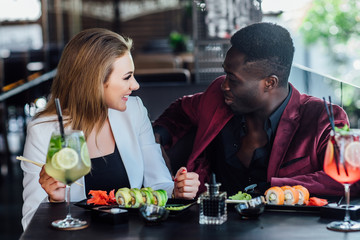Two young friends  having fun while eating sushi rolls in restaurant in modern terrace.