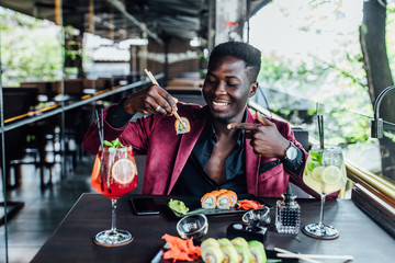 Portrait of african man holding chopsticks sushi rolls, Chinese food fish restaurant terrace. Healthy eat.
