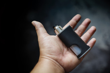 high end unregulated bottom feed squonk box mods with rebuildable dripping atomizer in hand on dark...