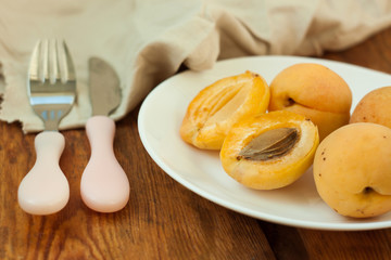 Ripe fresh apricot fruits on a white plate on the wooden background. Copy space, delisious healthy food.