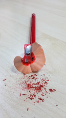 Red pencil and sharpener, isolated on wood background.