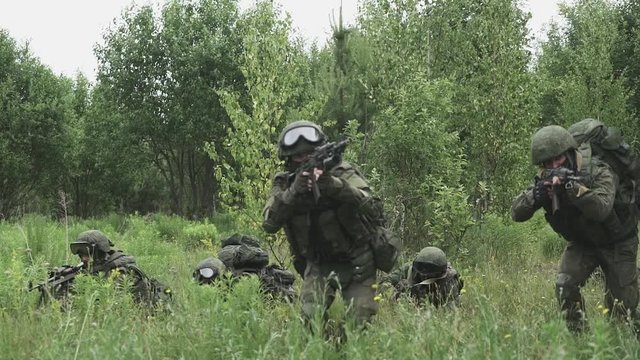Soldiers in camouflage with assault rifles, out of the ambush in the field, military action in the steppe area.