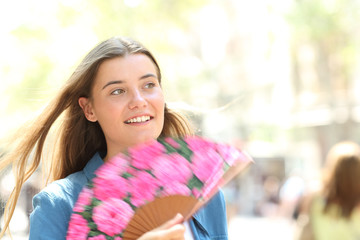 Happy woman using a fan walking in the street on summer