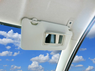 Car sun visor and mirror in car with sky and clouds as a backdrop.