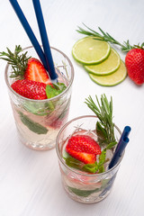 Strawberry mojito cocktail drink with with berries, lime, mint and rosemary on white wooden background