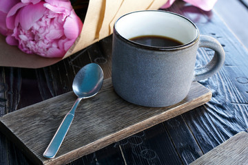 Cup of americano coffee with spoon on wooden surface and pink peonies flowers