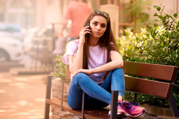 Beautiful young woman relaxing on the bench and making a call in the city