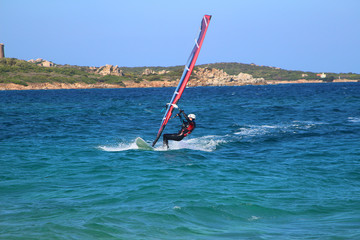 Young woman windsurfing in the beautiful backdrop of Sardinia (Vignola, Italy)