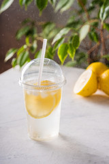 Ice lemonade with soda in plastic cup on the table with lemons and ice cubes. Refreshment drink.