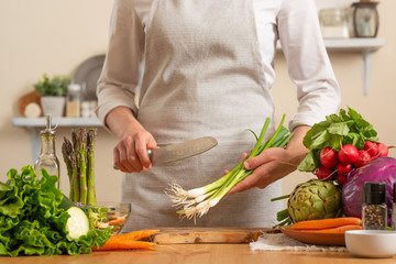 Chef cook with green onions, on a light background. The concept of losing healthy and wholesome food, detox, vegetarian food, diet, cooking. Slow food, comfort food, healthy diet, clean eating.