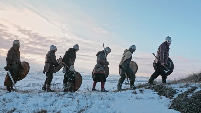 Group of medieval vikings with arms and shields going on the winter meadow.
