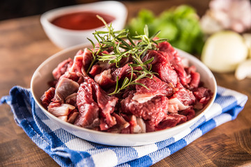 Raw beef pieces with rosemary in bowl on butcher board