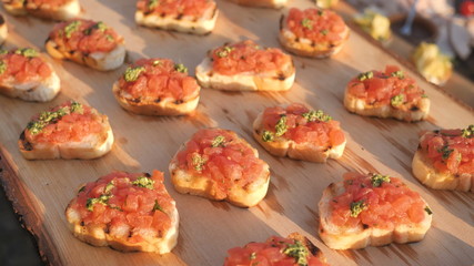 Delicious savory tomato Italian appetizers, or bruschetta, on slices of toasted baguette, decorated with natural basil, close-up on a wooden board catering service.