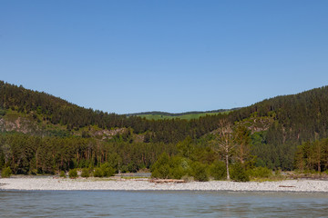 summer landscape on the river with stones and two mountains covered with green coniferous trees. travel and outdoor recreation.