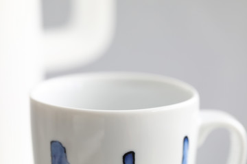 Empty white cup standing on table ready to be used with kettle in background