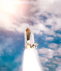 Dramatic launch. Rocket launching. Blue sky. CLouds and sun flare. Elements of this image furnished by NASA.