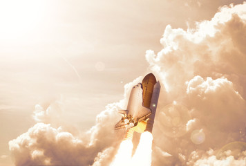 Spaceship taking off and flying high in blue sky. Clouds and smoke. Elements of this image...