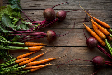 A bunch of carrots and beetroots . Fresh carrots, beetroot  heap with green stems. Raw Carrots on rustic  wooden background. Close up. top view 