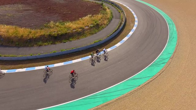 Aerial, tracking, drone shot,of a group of cyclists, bypassing others, on Autodromo do Estoril Circuit, at a 24 hour cycling competition, on a sunny day, near Lisbon, Portugal