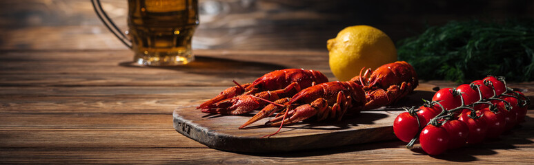 panoramic shot of red lobsters, tomatoes, dill, lemon and glass with beer on wooden surface