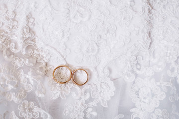 Obraz na płótnie Canvas Two wedding rings placed on a white wedding dress. Lace background.