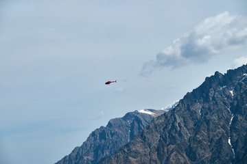 Naklejka na ściany i meble Red helicopter in the sky over the Caucasus Mountains, a beautiful mountain landscape.