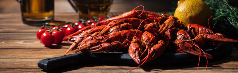 panoramic shot of red lobsters, tomatoes, dill, lemon and glasses with beer on wooden surface