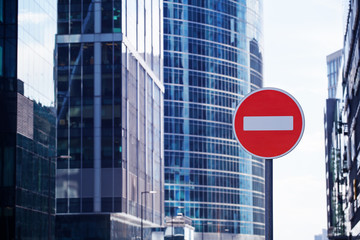 Red road stop sign or brick on city skyscrapers business center blurred background close up,...