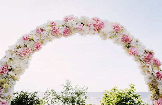 Wedding ceremony arch made of pink and white flowers. Sea and sky background.