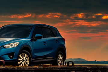 Blue compact SUV car with sport and modern design parked on concrete road by beach at sunset....