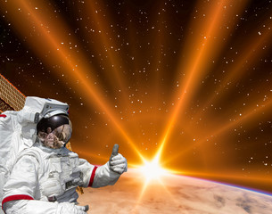 Planet earth and fascinating sunrise. Astronaut give thumbs up. The elements of this image furnished by NASA.