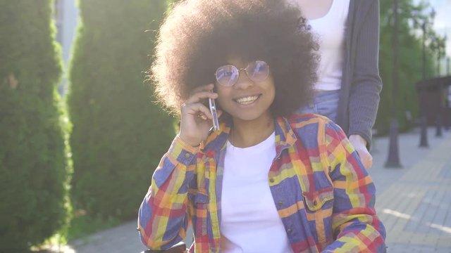 african woman with an afro hairstyle disabled in a wheelchair positive talking on the phone in the park