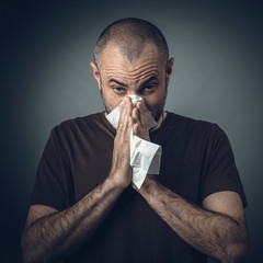 portrait of a man blowing his nose with a tissue. look at the camera.