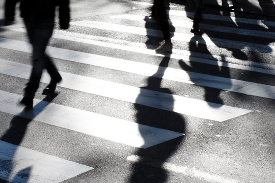 Fototapeta Blurry zebra crossing with pedestrians making long shadows