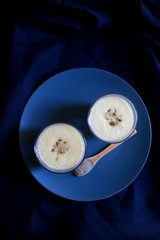 Two glasses of refreshing mango lassi drink, decorated with cardamom. Dark background, top view.