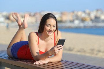 Happy teen in red using smart phone on the beach