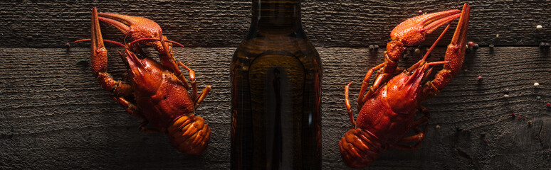 panoramic shot of red lobsters and glass bottle with beer on wooden surface