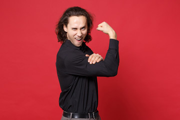 Handsome stylish young curly long haired man in black shirt posing isolated on red background studio portrait. People sincere emotions lifestyle concept. Mock up copy space. showing biceps, muscles.