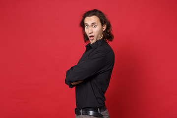 Young sad curly long haired man in black shirt standing posing isolated on red wall background studio portrait. People sincere emotions lifestyle concept. Mock up copy space. Problem crisis depression