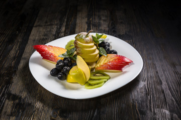 Low key restaurant menu food photo. Delicious fresh shoped fruits in white plate on a dark rustic wooden background