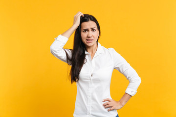 Portrait of preoccupied worried young woman in white shirt looking camera putting hand on head isolated on bright yellow orange wall background in studio. People lifestyle concept. Mock up copy space.