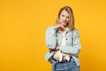 Portrait of confident smiling young woman in denim casual clothes put hand prop up on chin, looking camera isolated on yellow orange background in studio. People lifestyle concept. Mock up copy space.