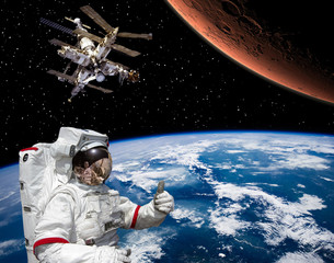 Astronaut shows the thumbs-up about flying to Mars. Space station on the backdrop. The elements of...