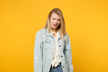 Portrait of perplexed irritated young woman in denim casual clothes standing, looking camera isolated on bright yellow orange wall background in studio. People lifestyle concept. Mock up copy space.